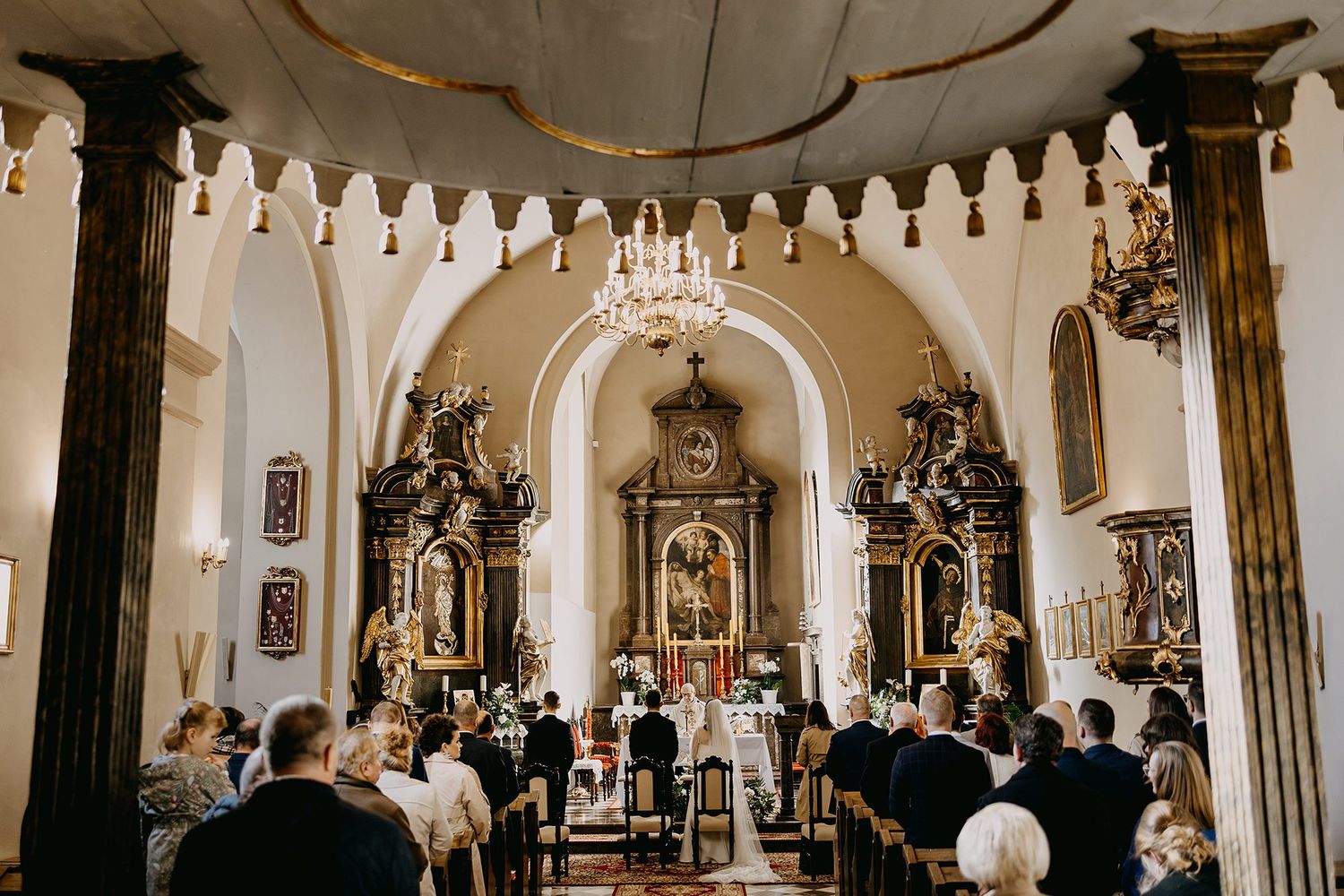 Guests attend a traditional Catholic wedding ceremony inside an ornate historic church with baroque altars.