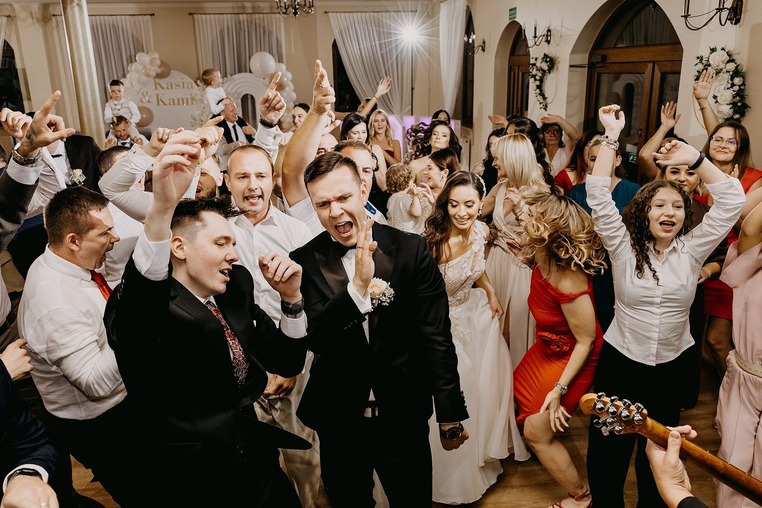 Excited wedding guests and groom celebrating joyfully on the dance floor at reception party.