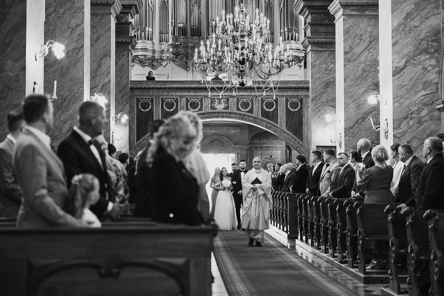 Black and white photo of wedding ceremony inside ornate church with chandelier.