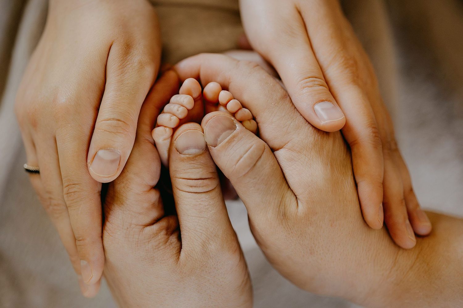 Close-up of two adult hands gently cradling tiny newborn baby feet in a tender moment.