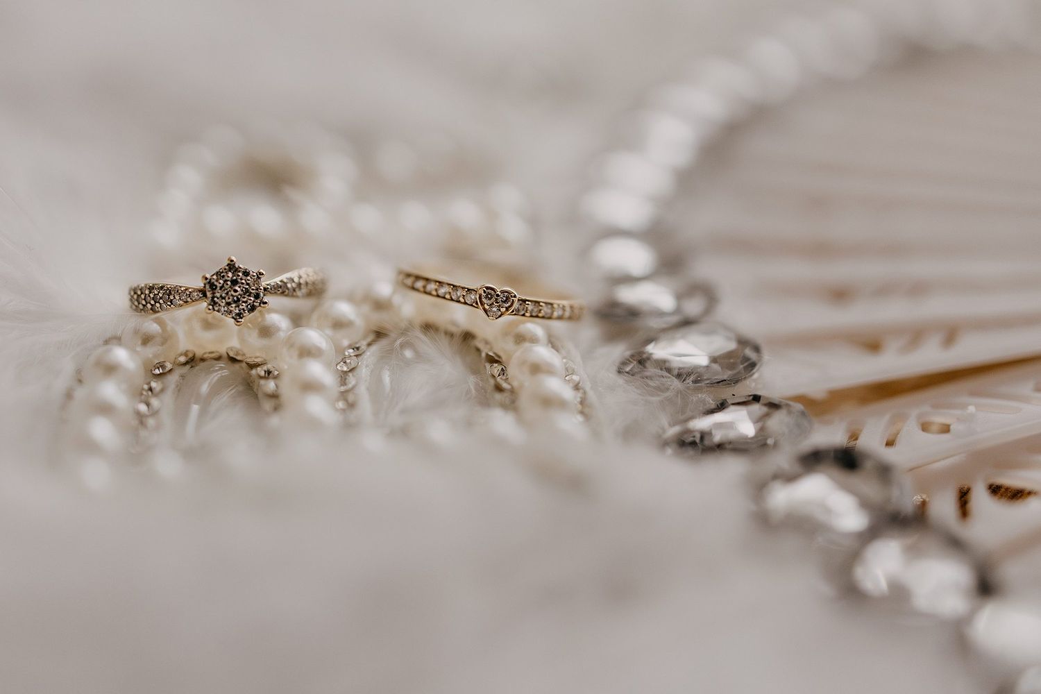 Close-up of a delicate diamond engagement ring resting on pearls and crystal jewelry.