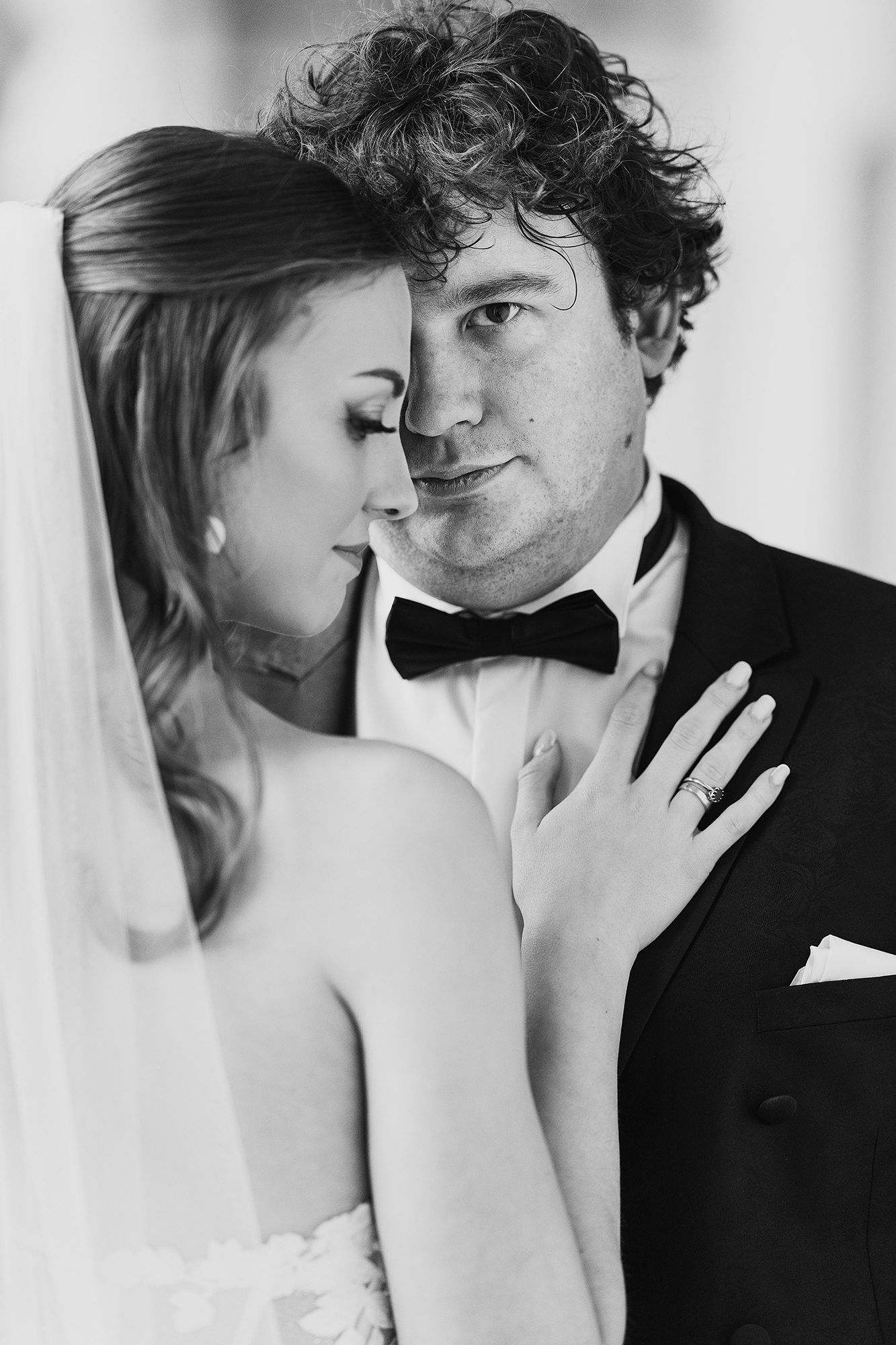 Black and white portrait of bride leaning into groom in a tuxedo with bow tie.