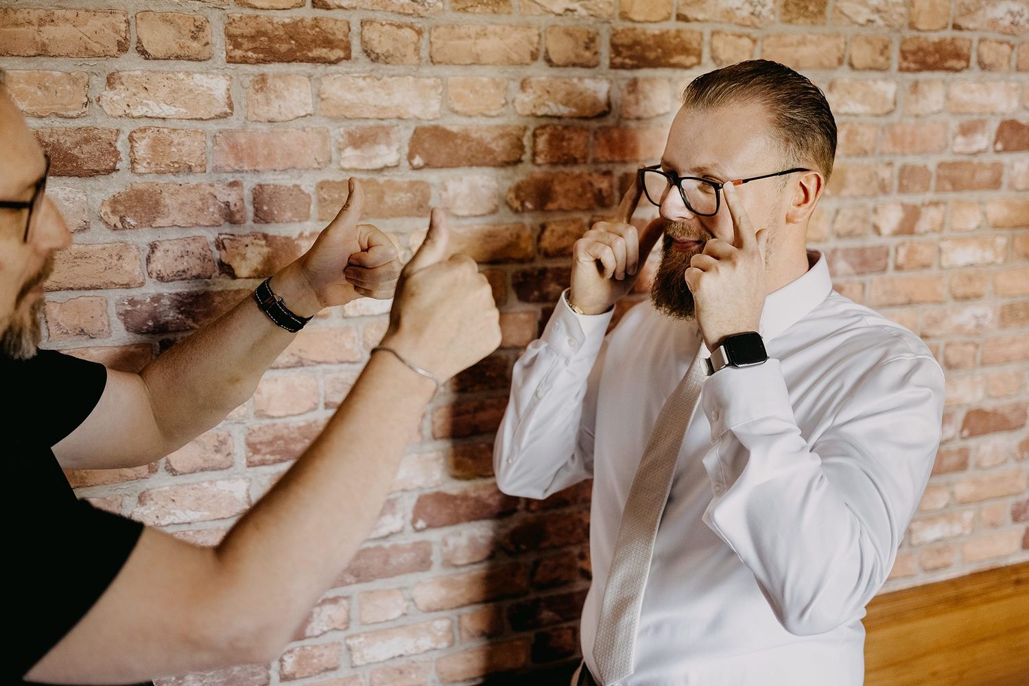 Groom adjusting glasses while getting ready against exposed brick wall.