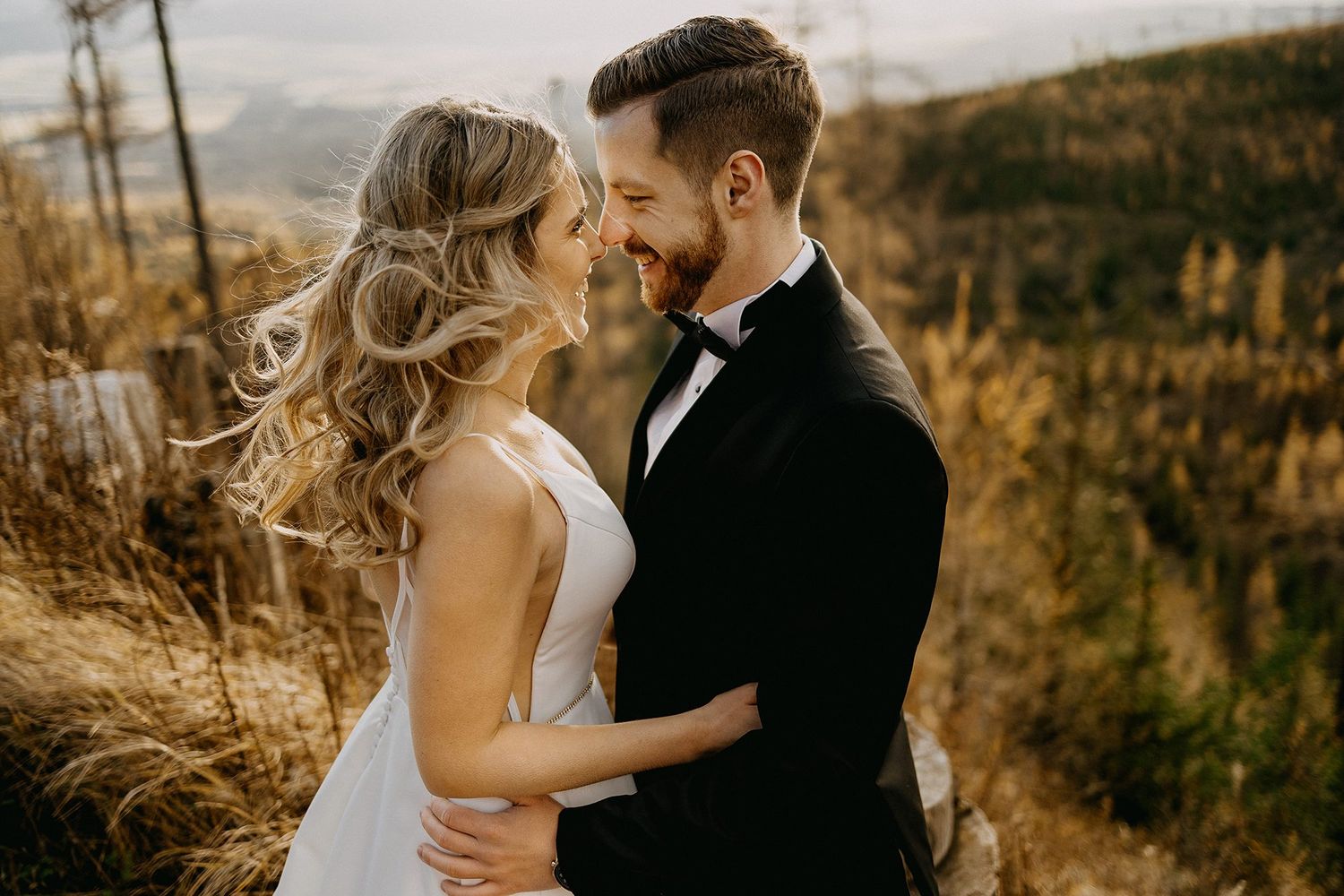Bride and groom share a romantic moment outdoors in a golden autumn mountain setting.