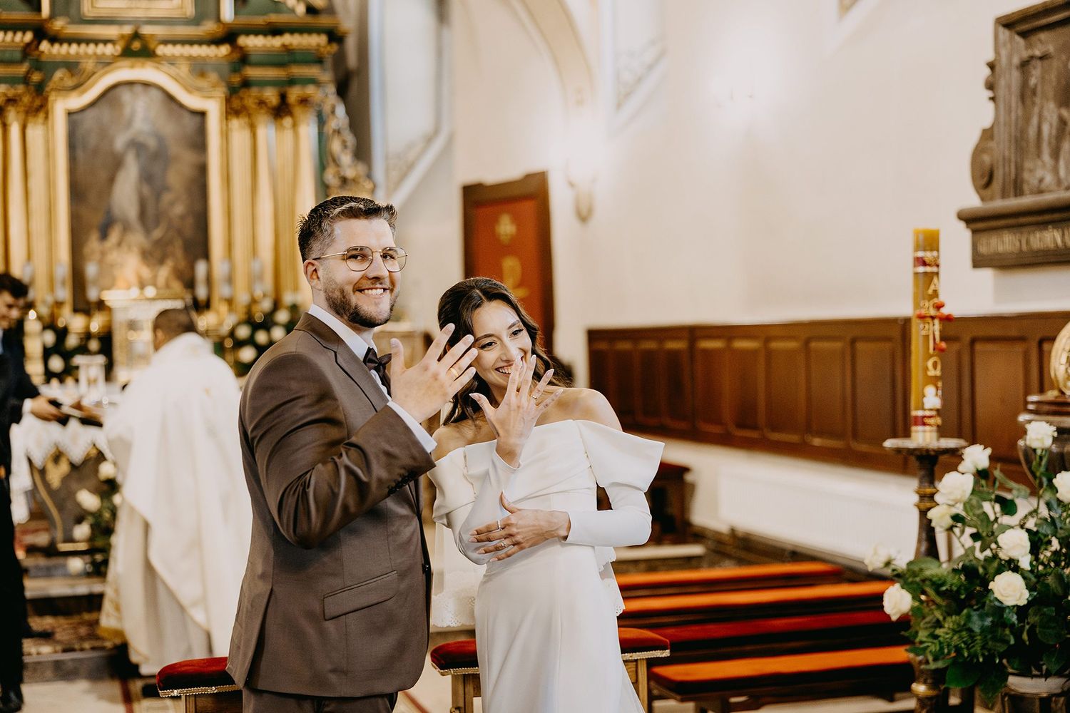 Bride and groom exchange rings during church wedding ceremony, both smiling joyfully at the altar.