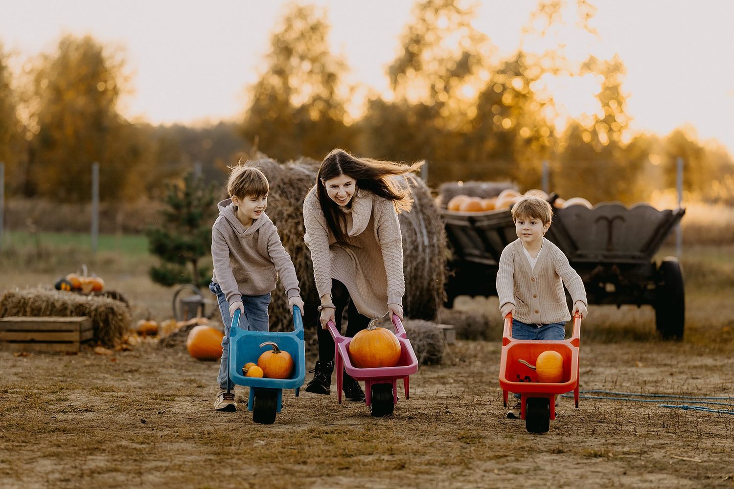 Mother and two children pushing wheelbarrows with pumpkins at a fall harvest farm.