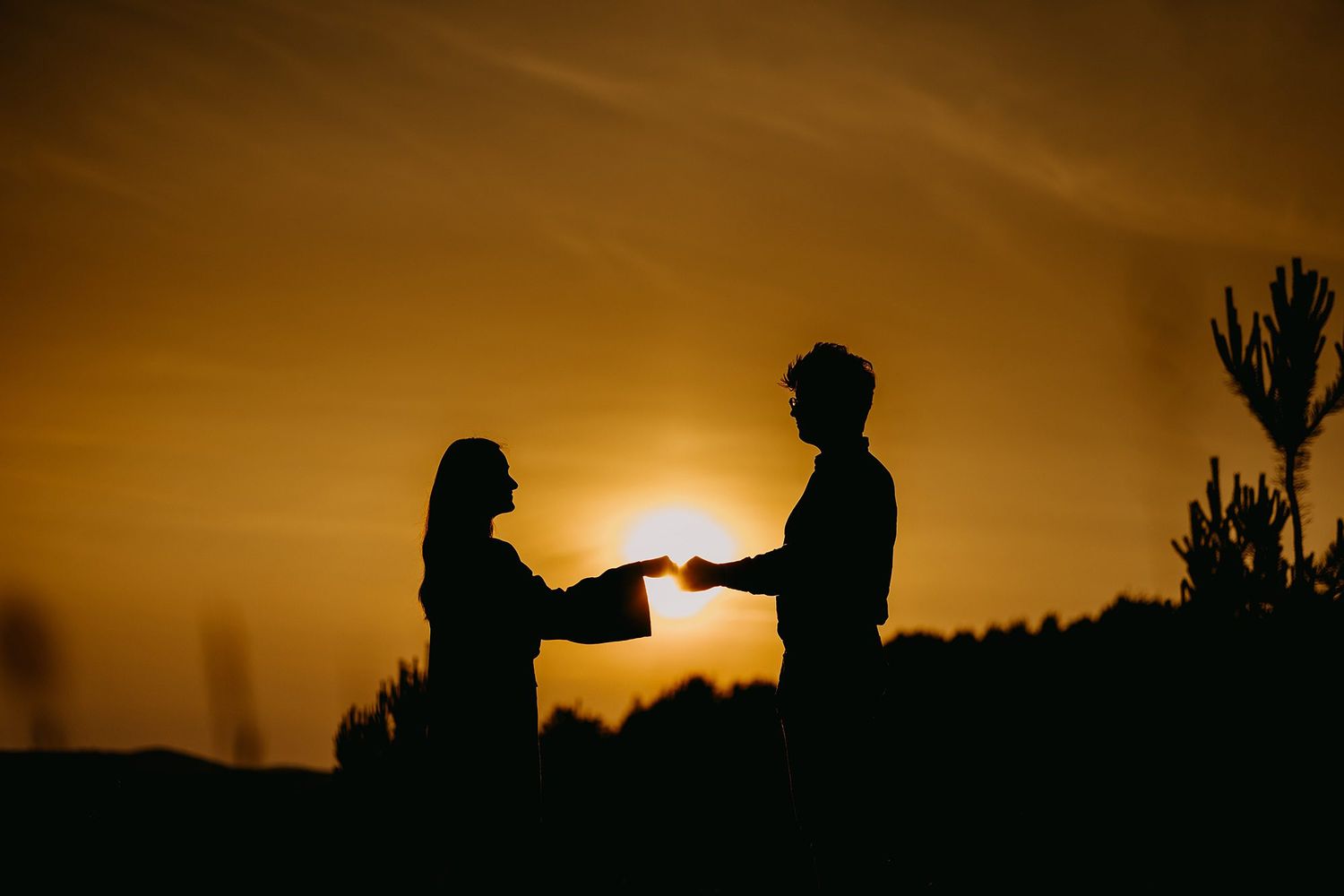 Romantic silhouette of couple holding hands at sunset with golden sky background.
