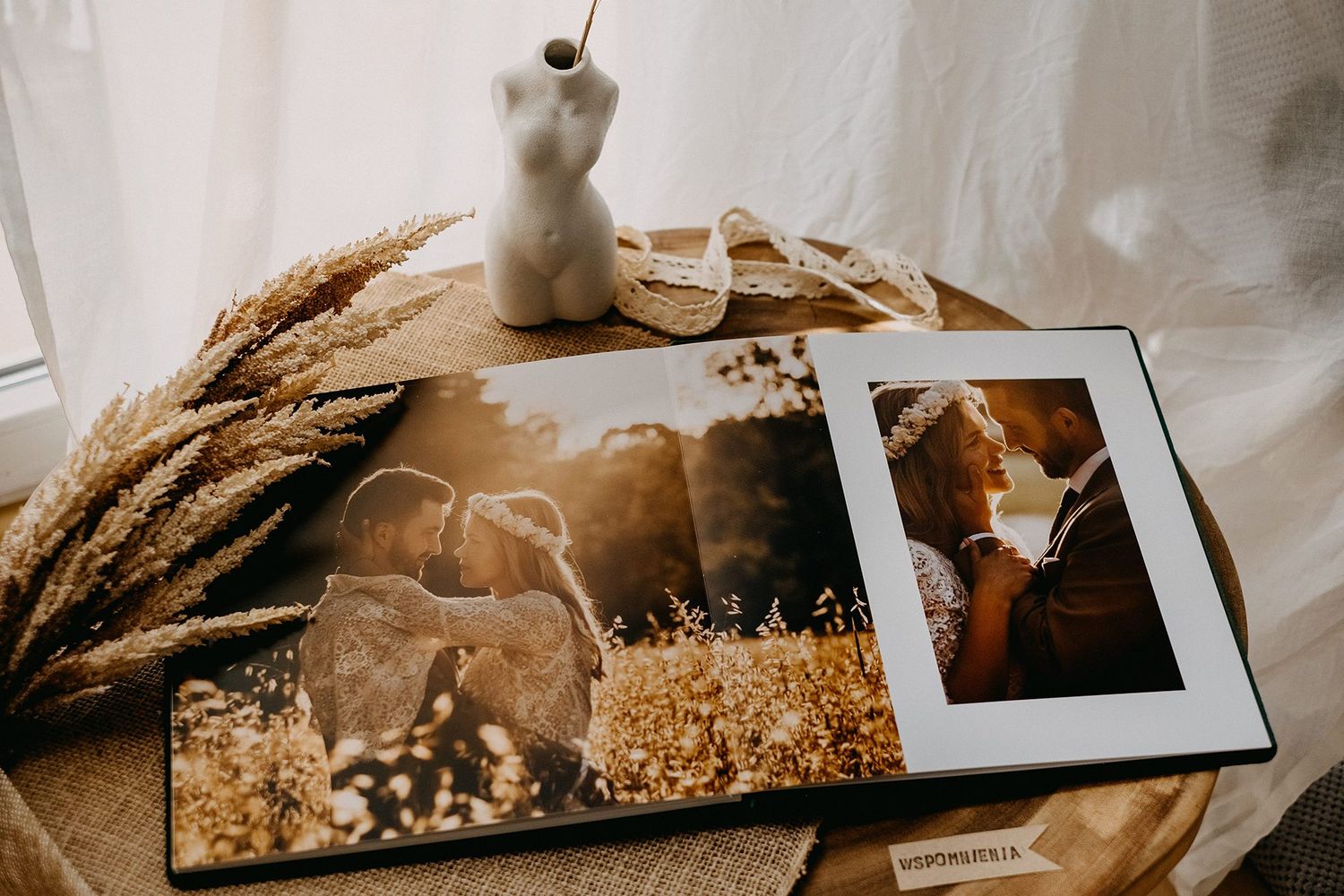 Open wedding photo album displaying romantic couple portraits in golden wheat field on rustic wooden surface.