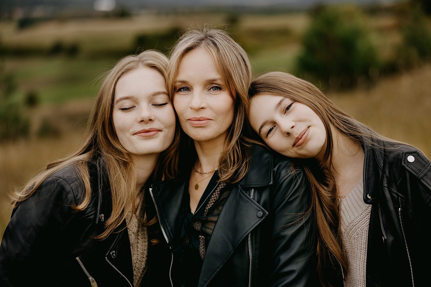 Mother and two teenage daughters in black leather jackets outdoors.
