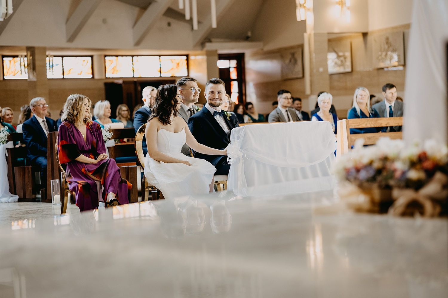 Bride and groom seated at church altar during wedding ceremony with guests in pews.