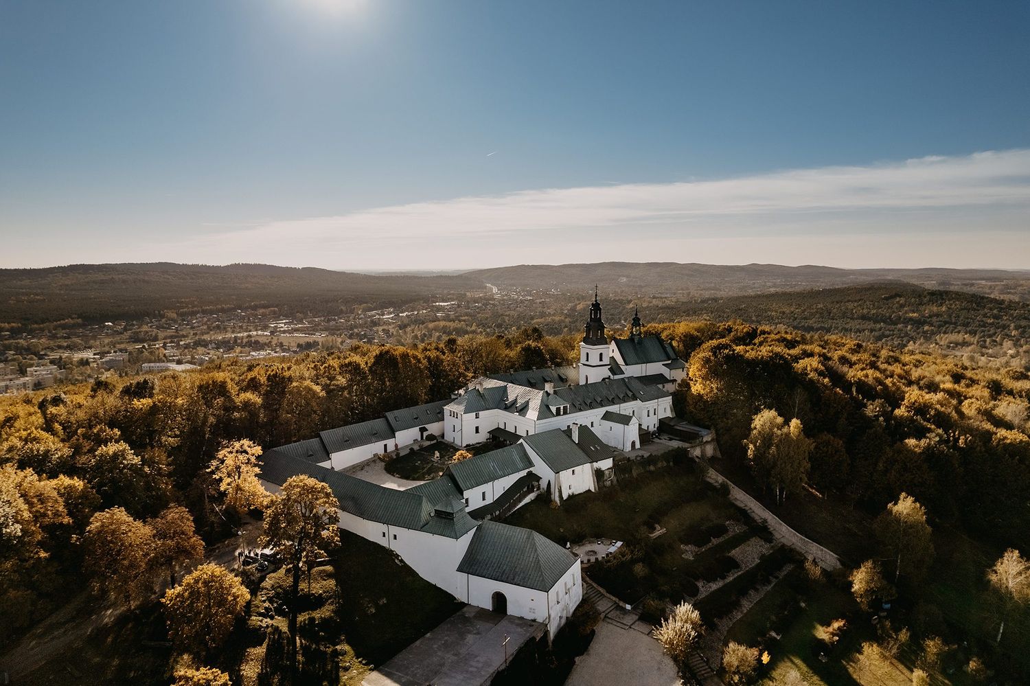 Aerial view of a historic monastery surrounded by autumn trees and rolling hills.