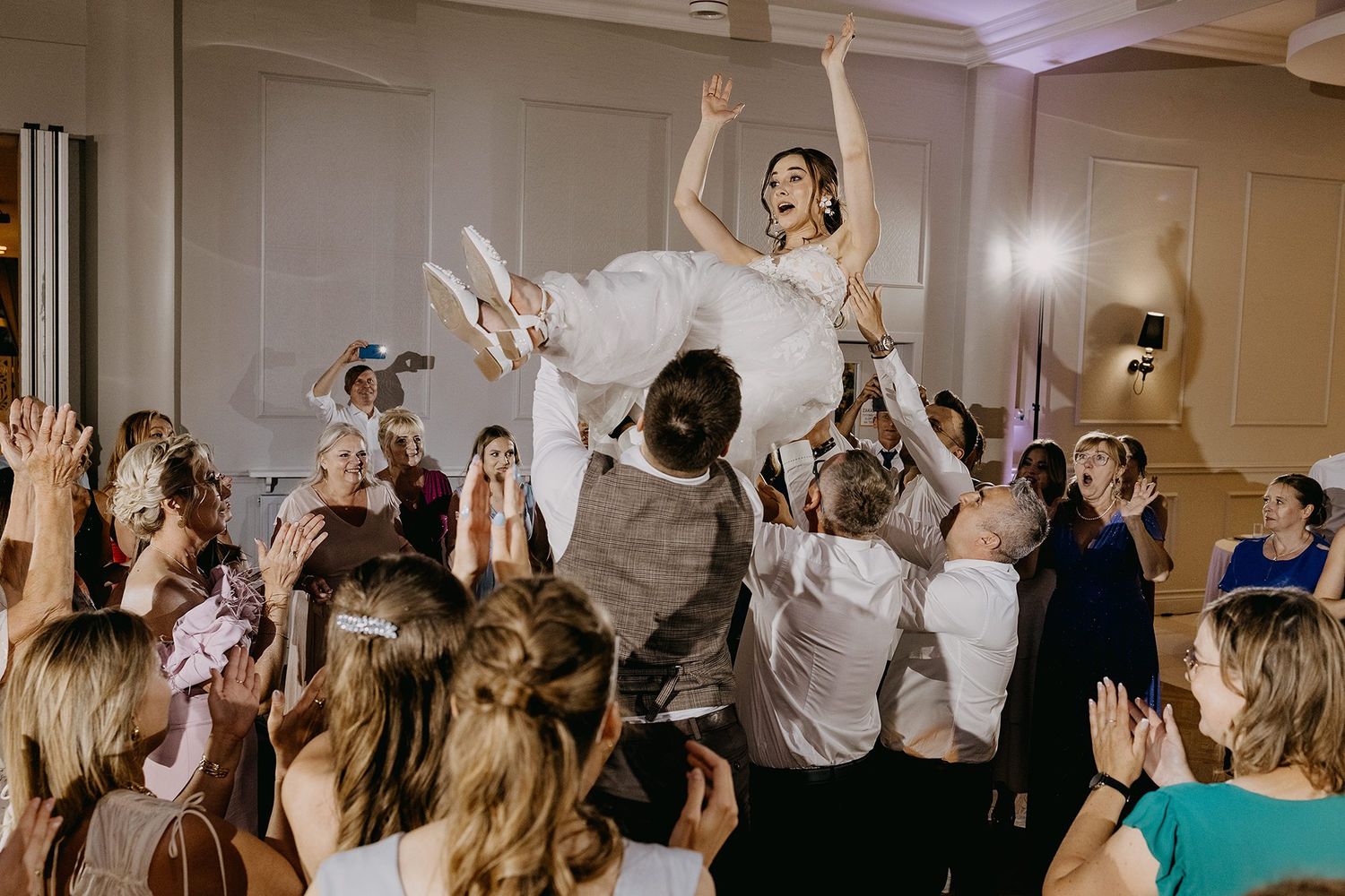Bride lifted by wedding guests during energetic celebration on the dance floor.