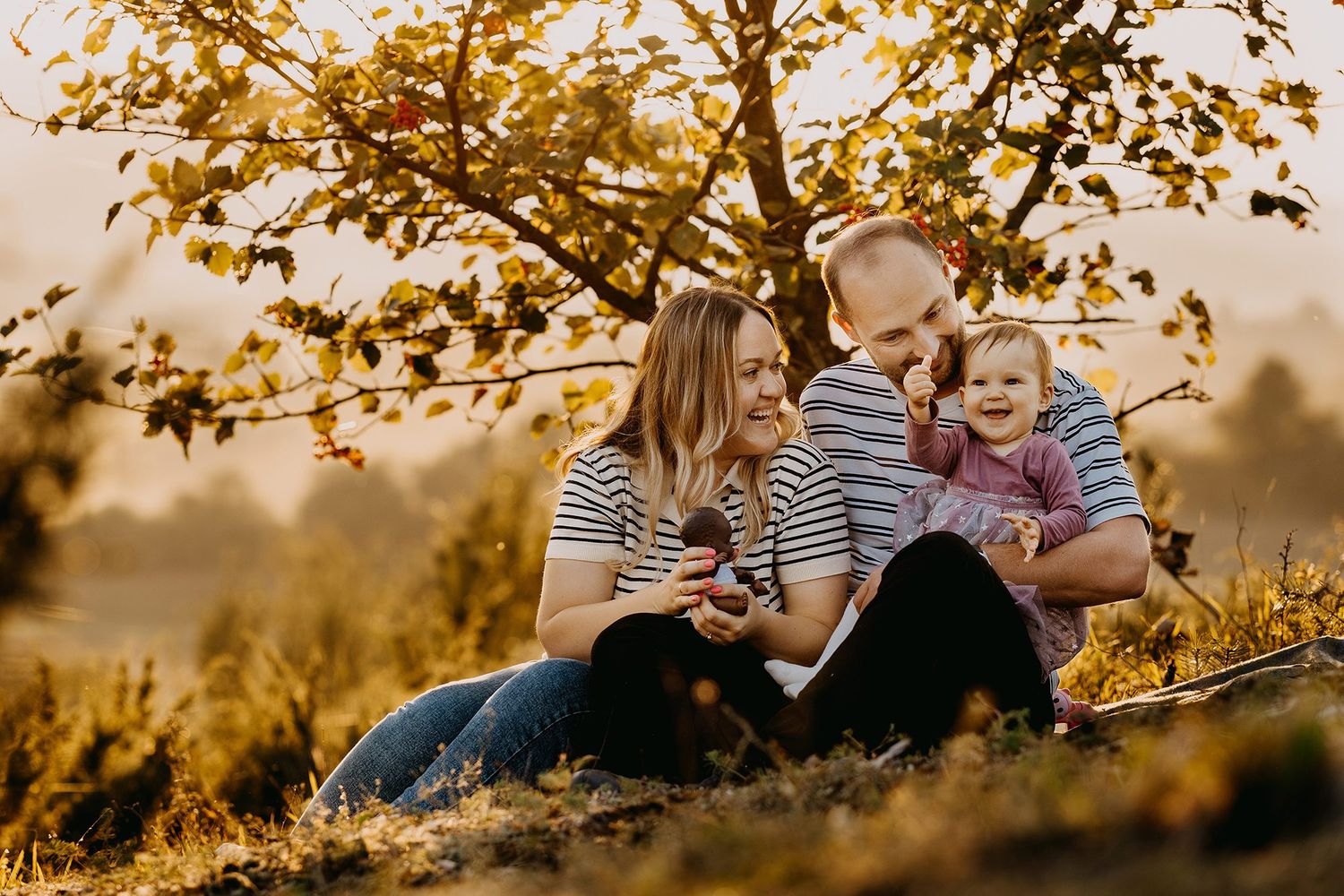 Joyful family sitting together under autumn tree in warm golden sunset light.
