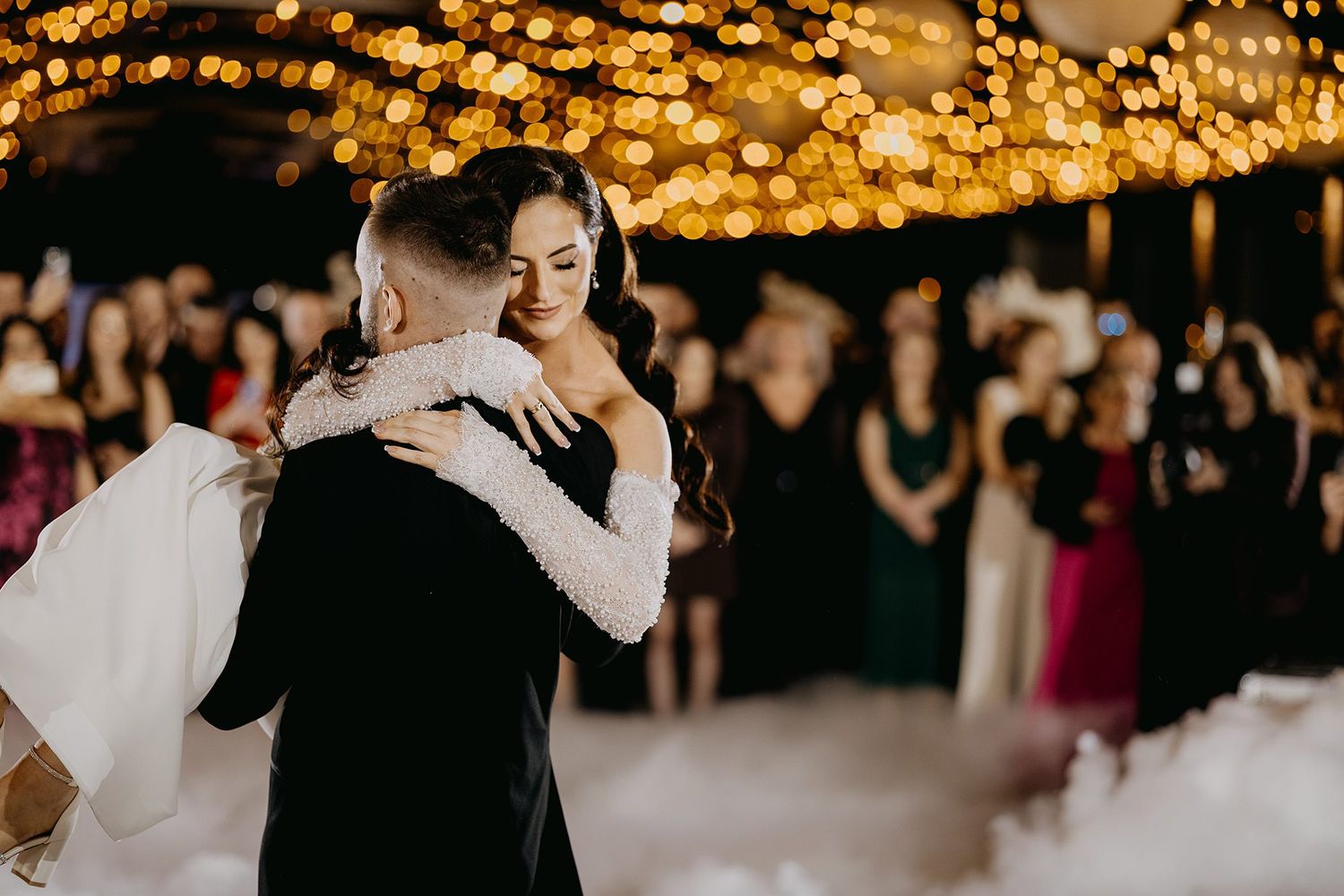 Bride and groom share their first dance surrounded by fairy lights and fog at an elegant wedding reception.