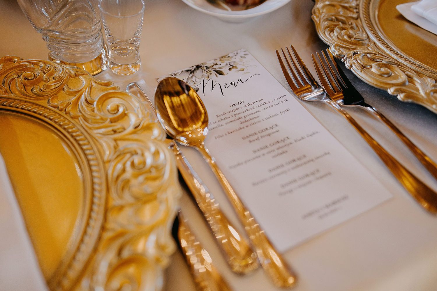 Elegant wedding table setting with ornate gold charger plates, gold cutlery, and a decorative menu card.