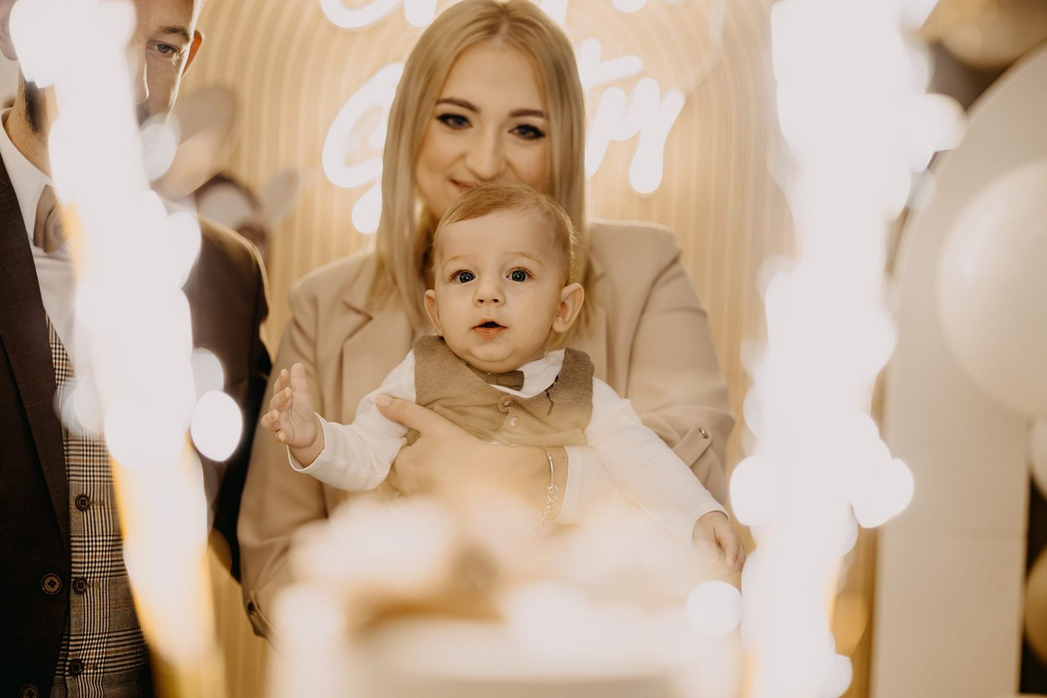 A smiling mother holds her baby surrounded by sparklers at a christening celebration.