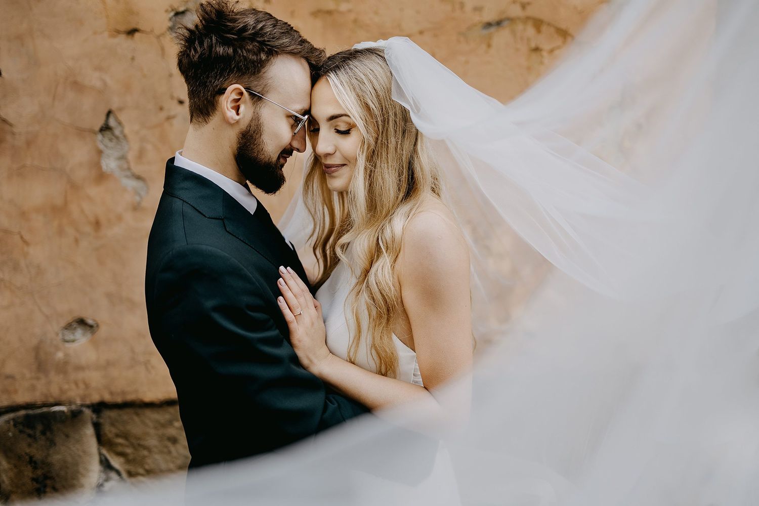 Groom and bride nearly kissing with flowing veil in foreground.