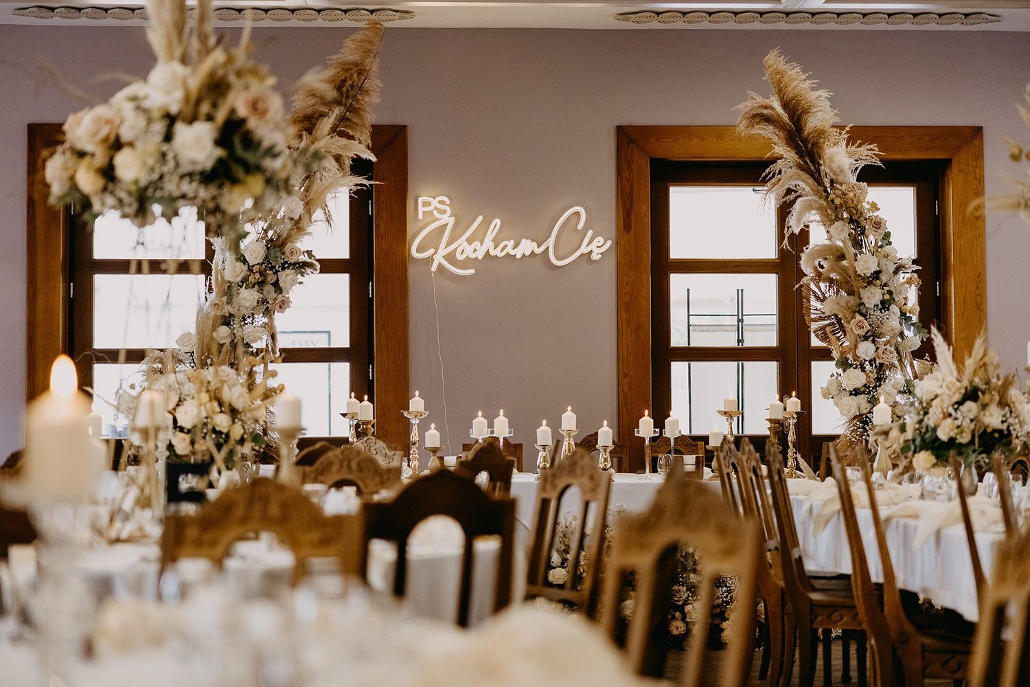 Boho wedding reception with pampas grass, floral arches, neon sign, and neutral-toned decor on long dining table.