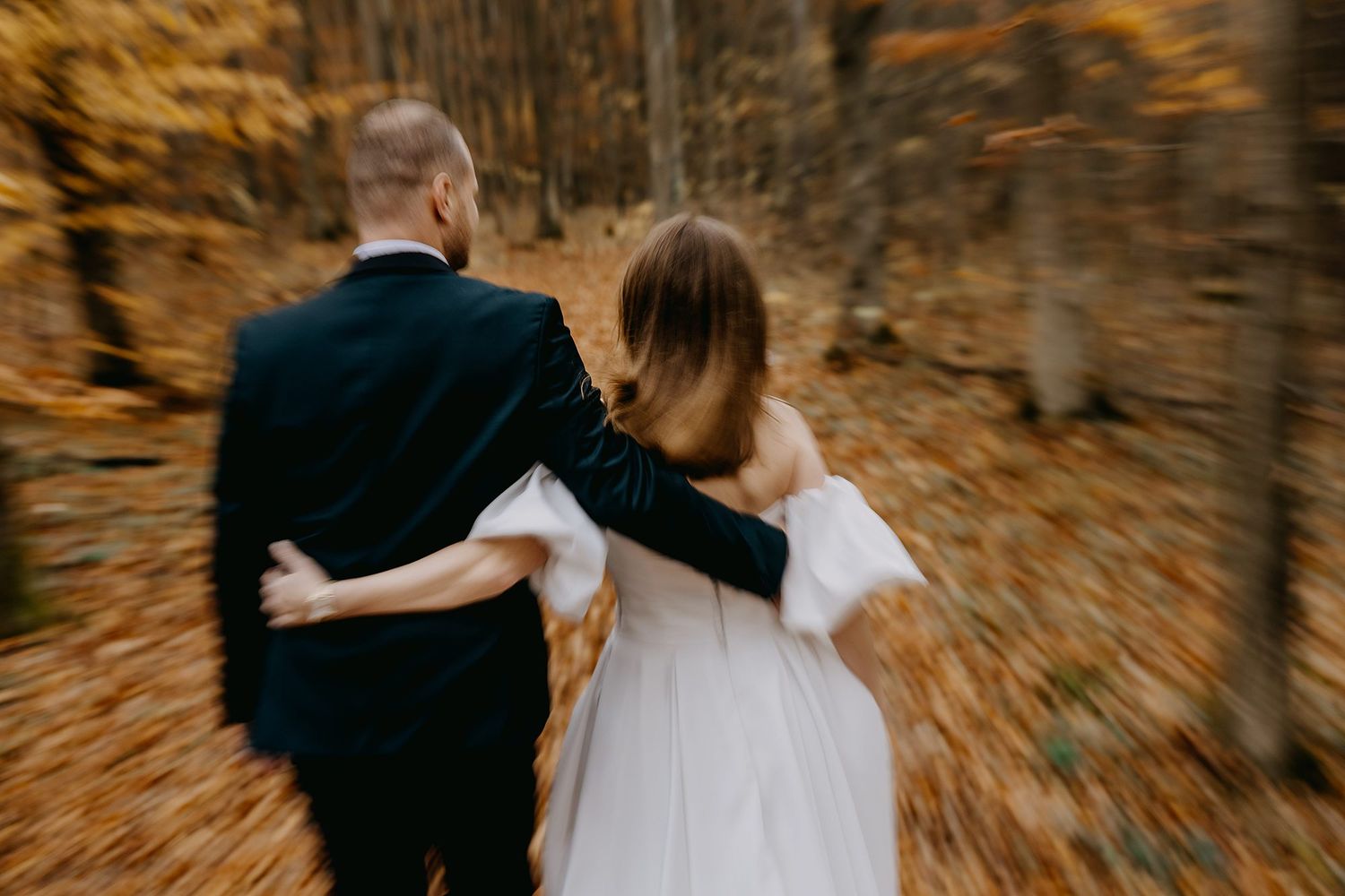 Bride and groom walk arm in arm through vibrant golden autumn forest, motion blur effect.