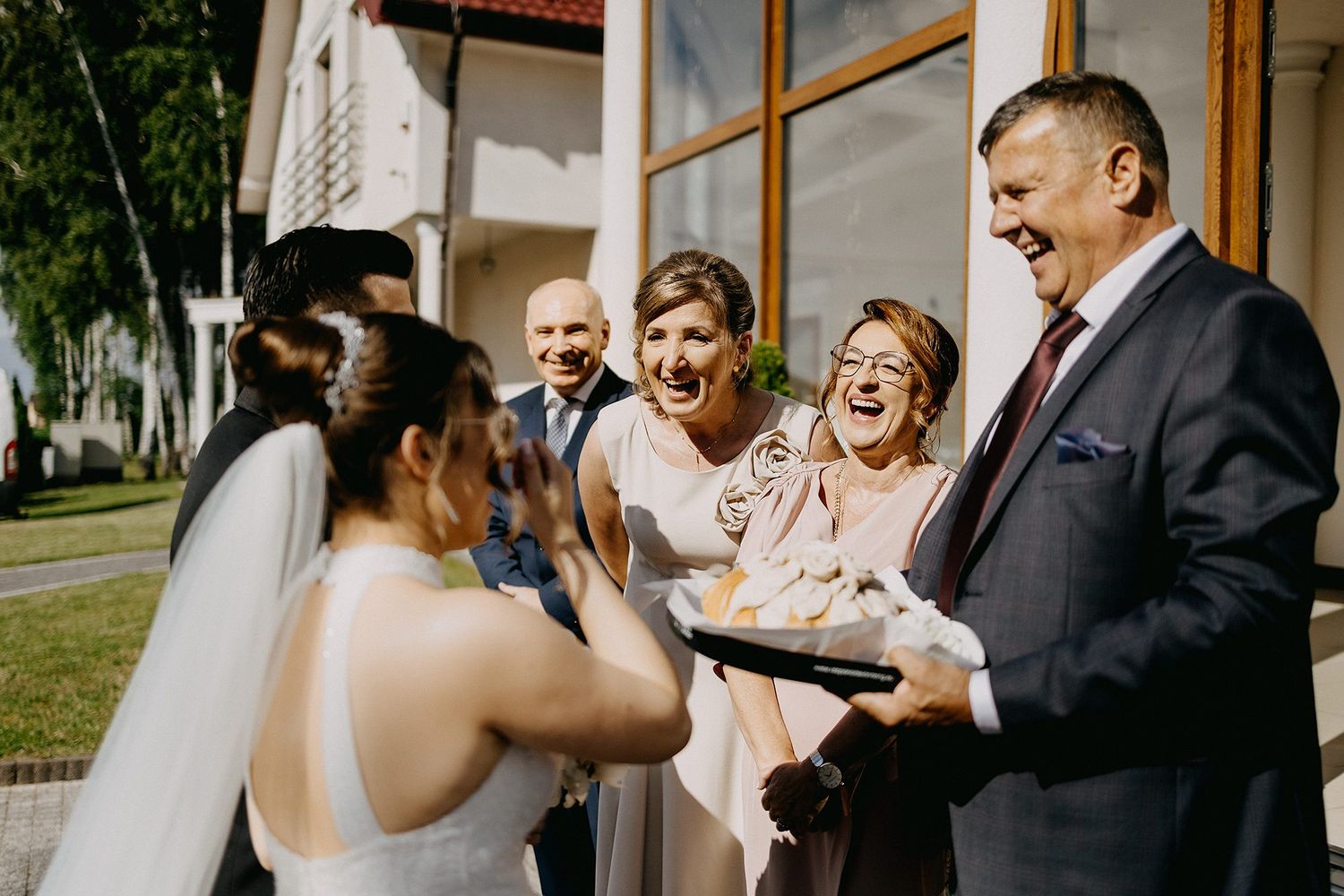 Wedding guests laughing and celebrating with the bride during a traditional bread and salt ceremony.
