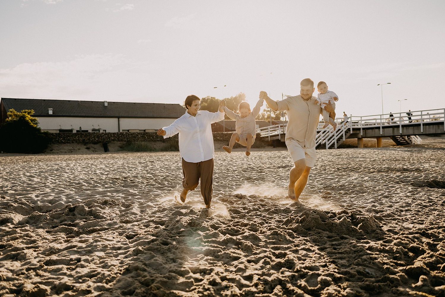 Joyful family playing together on a sandy beach at golden sunset, children jumping with excitement.