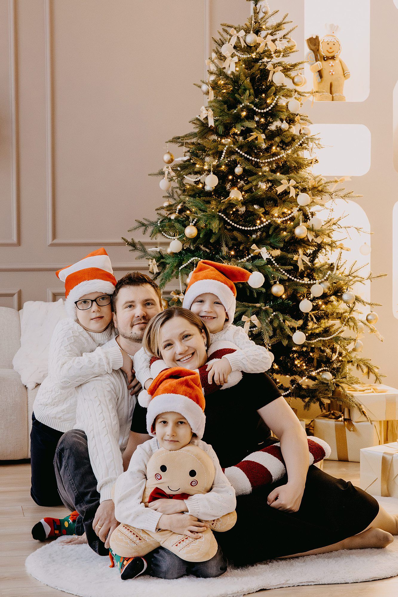 Happy family of five wearing Santa hats sitting together in front of a decorated Christmas tree.
