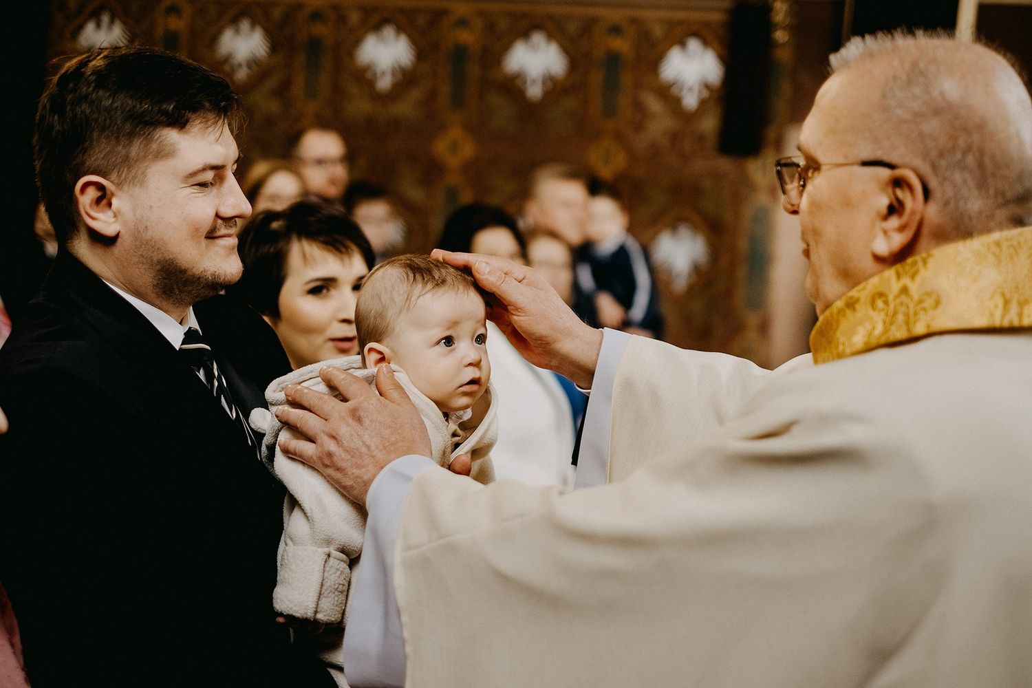 Priest blesses baby during christening ceremony as proud parents hold child at altar.