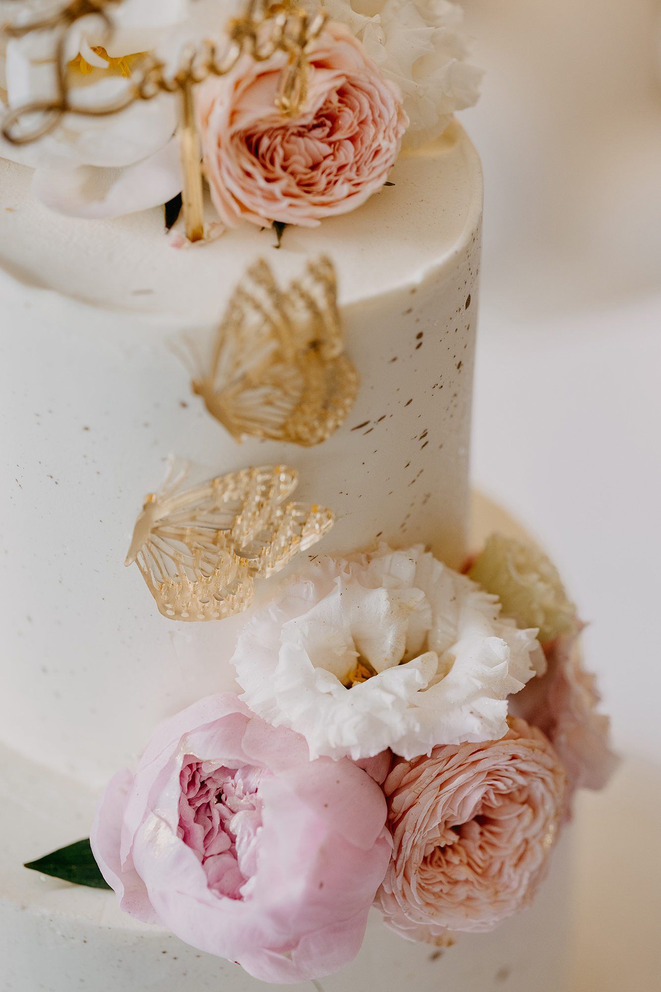 Elegant white christening cake decorated with pink peonies, roses, and gold butterfly ornaments.