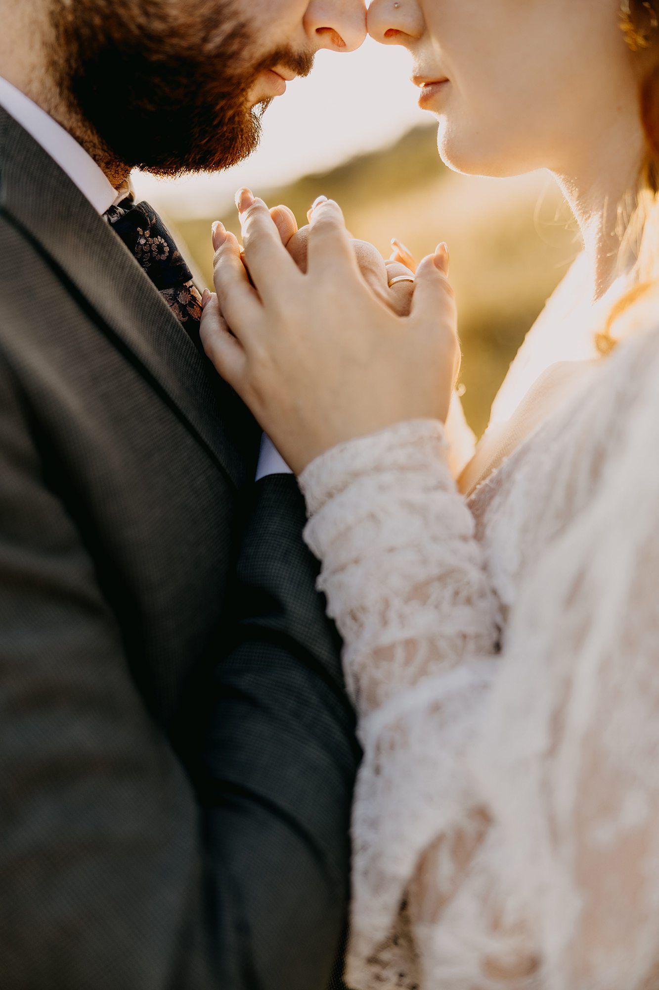 Bride and groom holding hands close up at golden hour, bride wearing lace dress and engagement ring.
