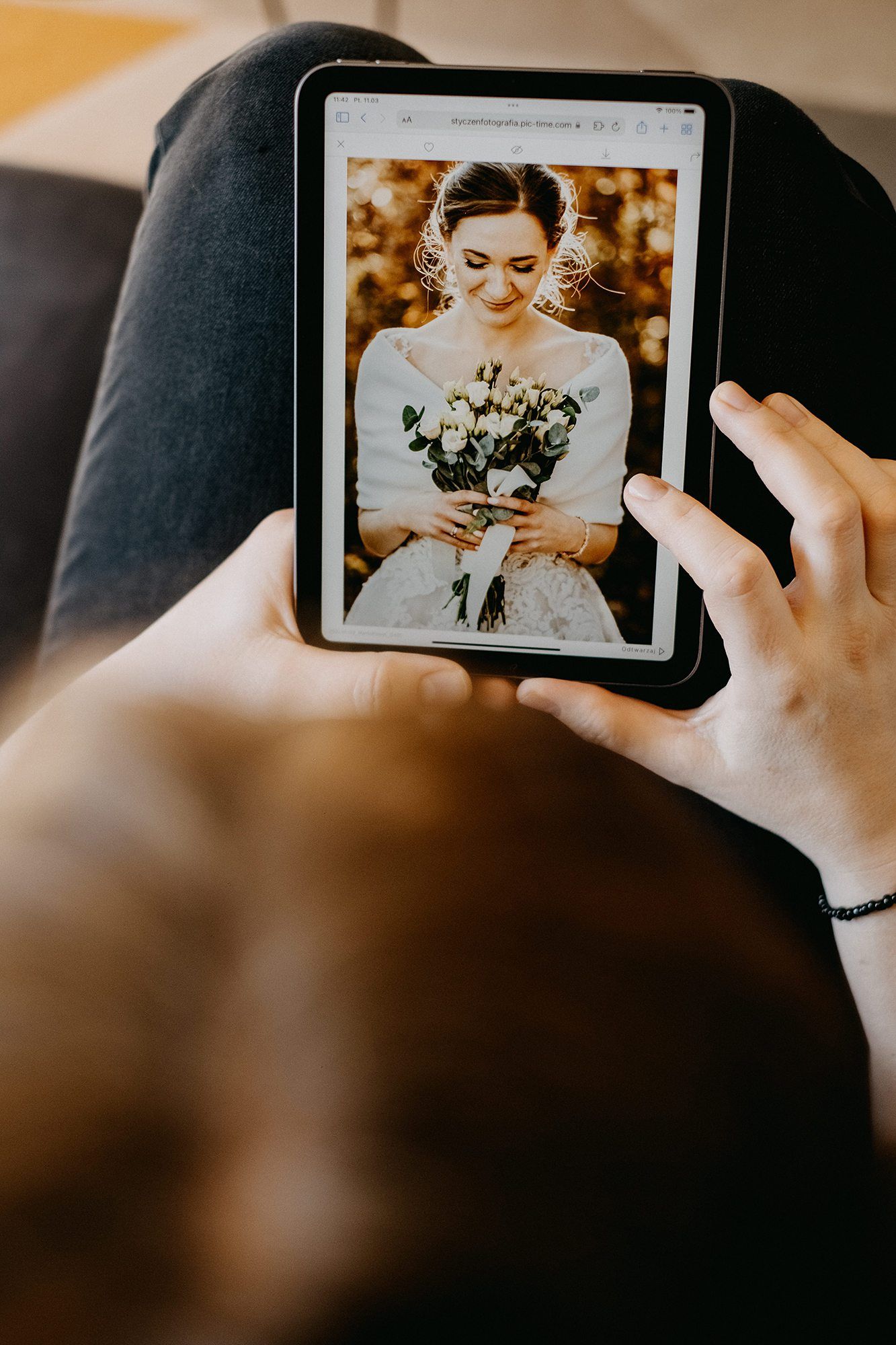 Person viewing a smiling bride holding white flowers bouquet on a tablet screen.