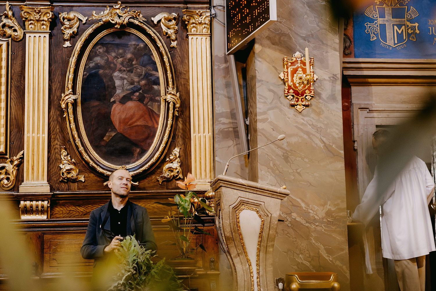 Person standing near ornate golden altar with oval painting in an elegant historic church interior.