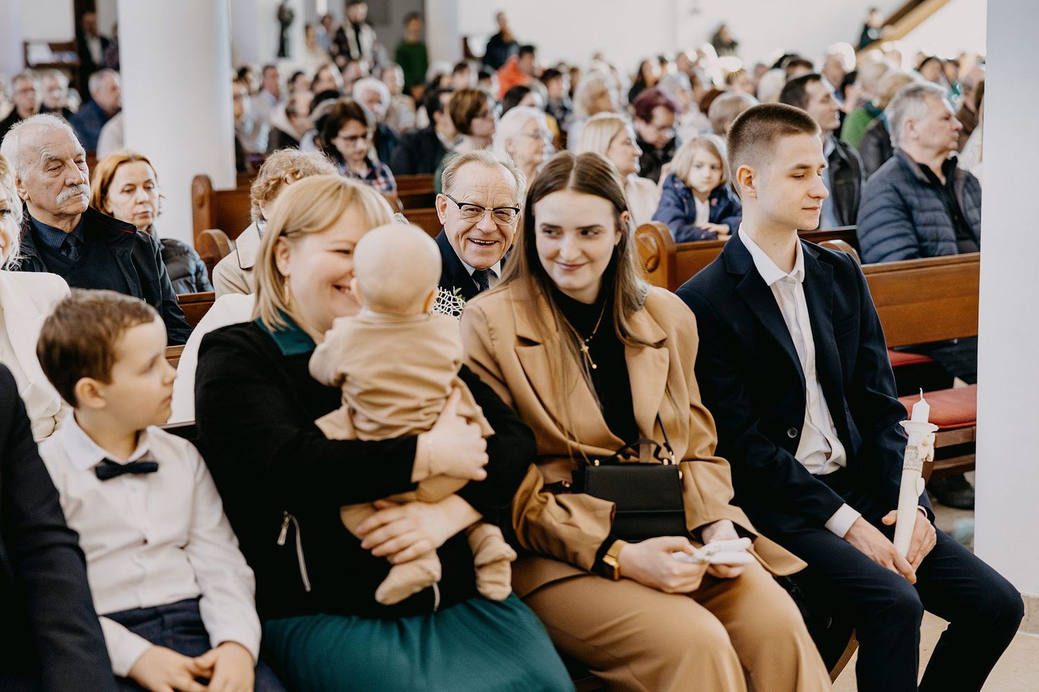 Family group with laughing baby seated in church pews during baptism service.