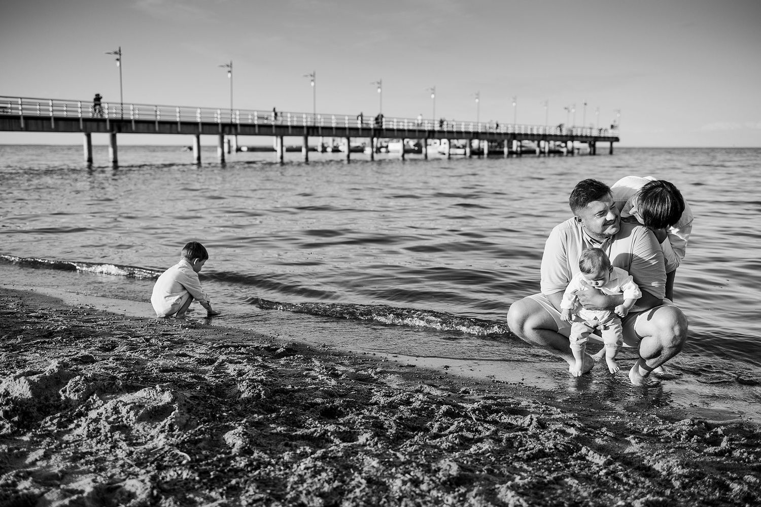 Black and white photo of family with young children playing at the shoreline.