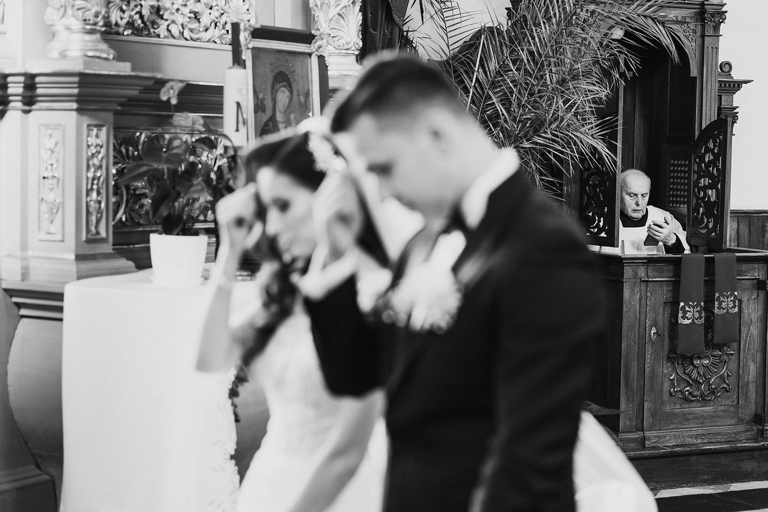 A bride and groom wipe away tears during an emotional black and white wedding ceremony in a church.
