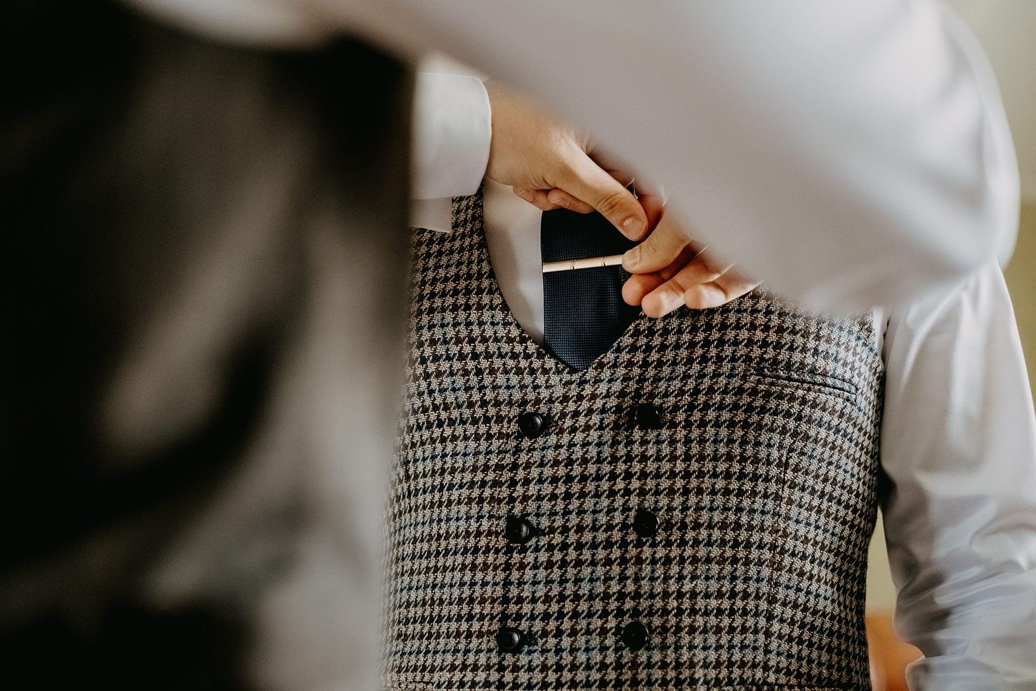 Close-up of hands adjusting a boutonniere on a houndstooth vest before a wedding.