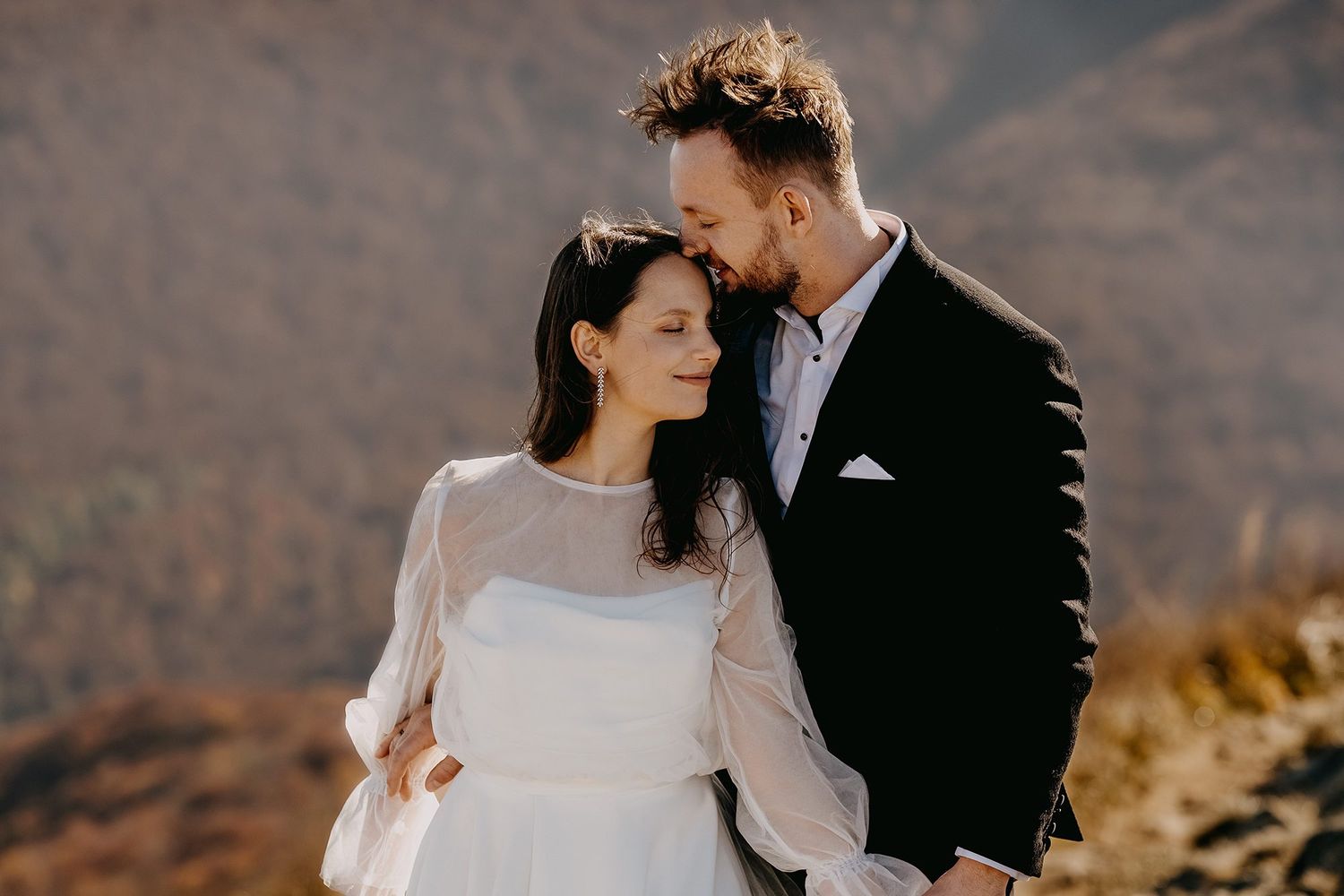Bride and groom sharing an intimate moment with warm sunlight illuminating a mountain backdrop.