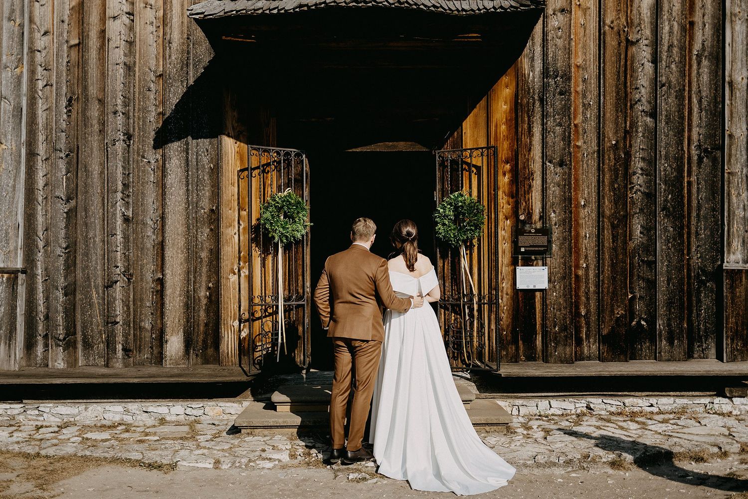 Bride and groom standing before rustic wooden barn wedding venue entrance.
