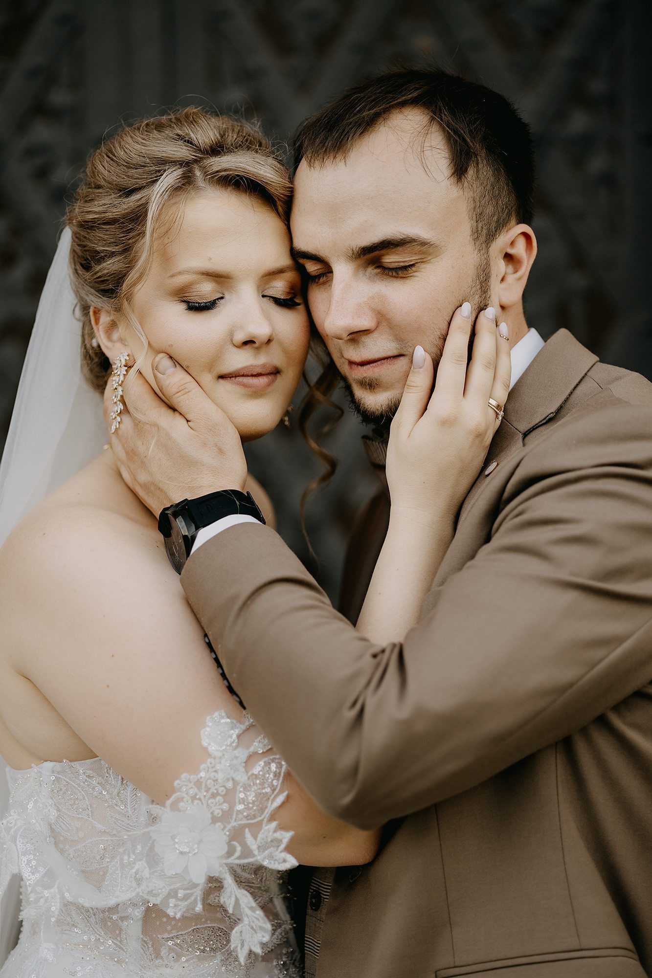 Bride and groom tenderly cradle each other's faces in an intimate close-up wedding portrait.