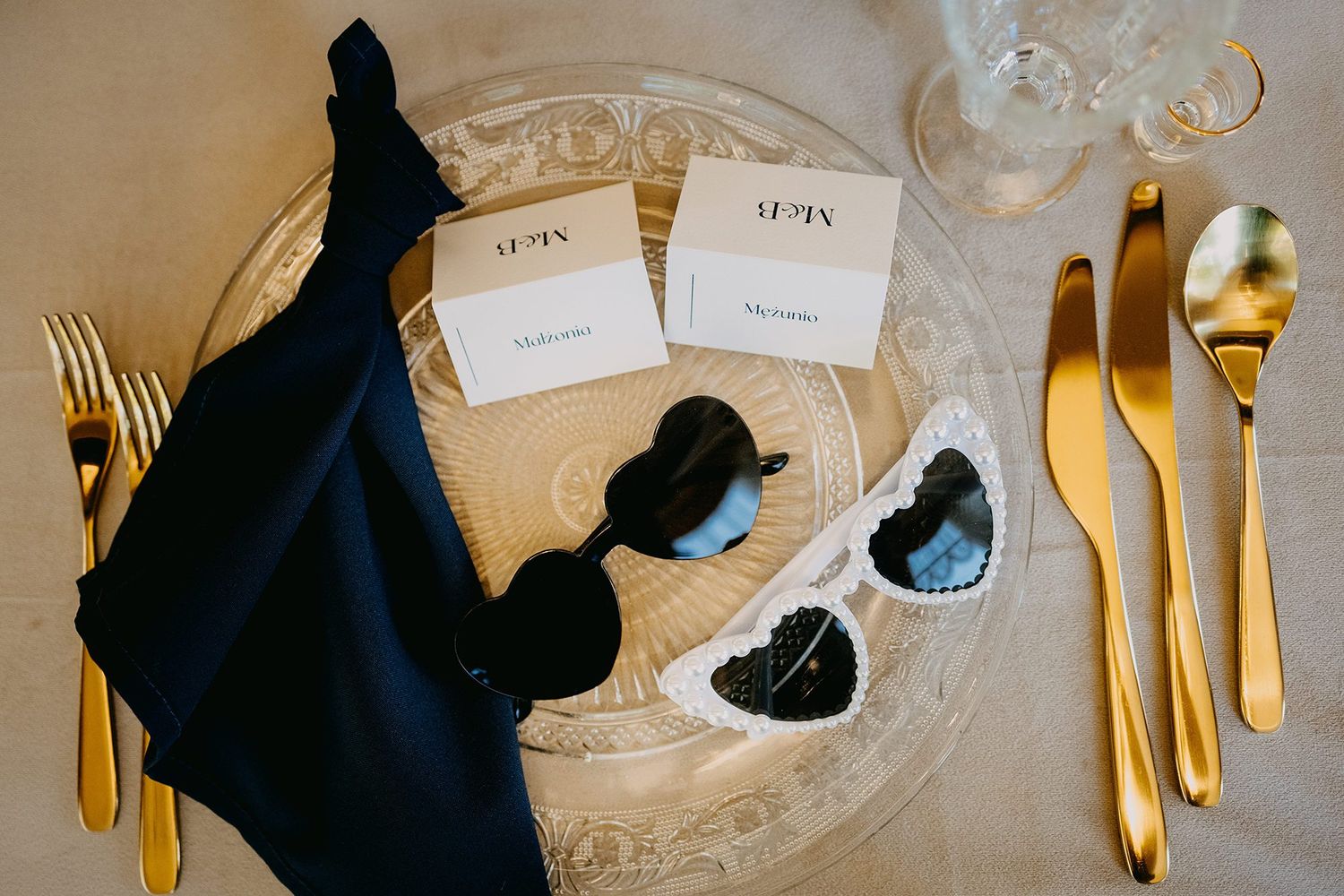 Elegant wedding table setting with gold cutlery, sunglasses, and personalized place cards.