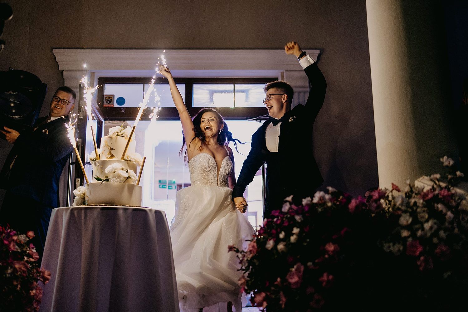 Bride and groom celebrating with sparklers beside wedding cake at elegant evening reception.
