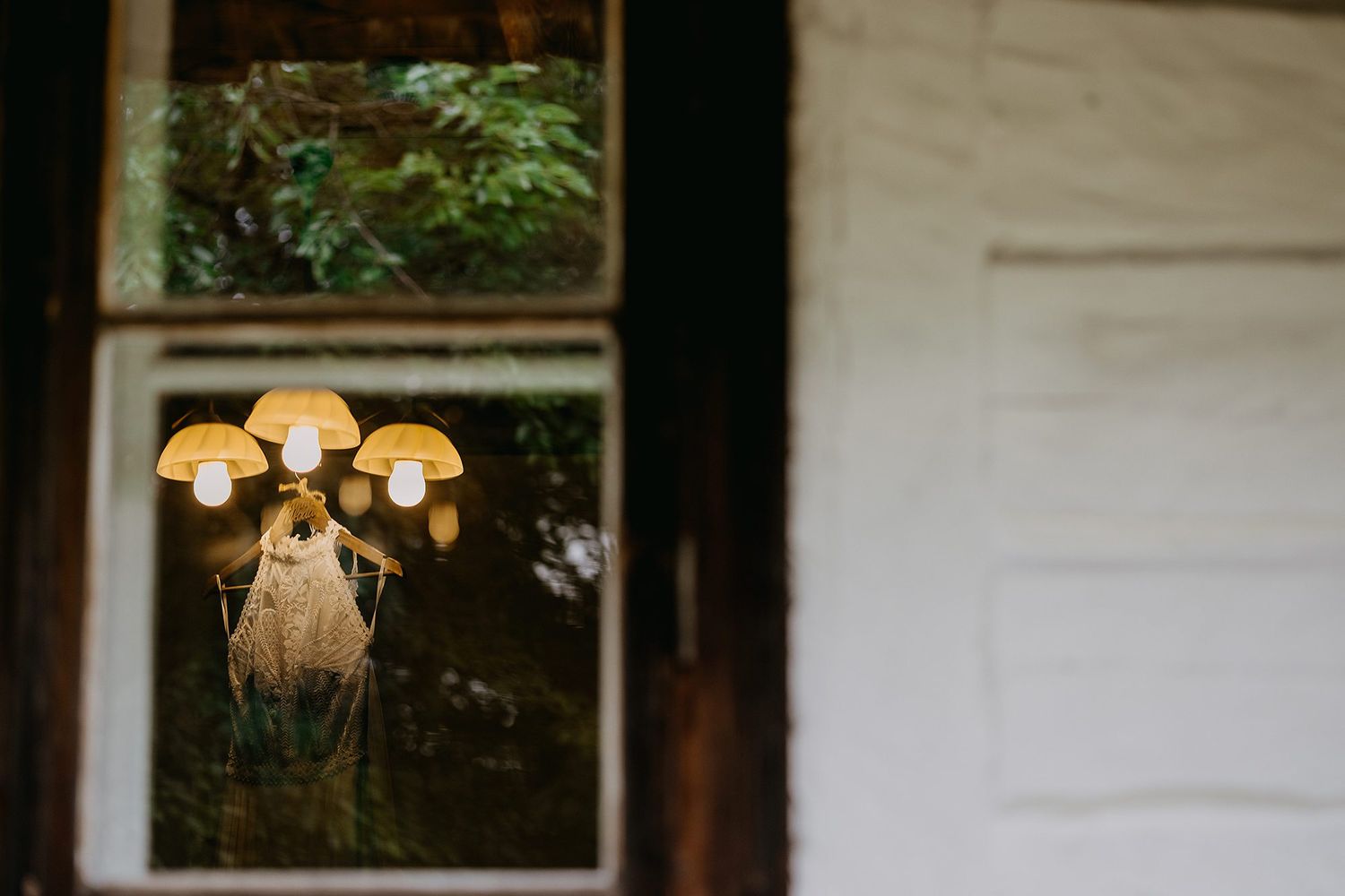 Vintage mushroom-shaped lamp cluster reflected in old wooden window frame surrounded by greenery.