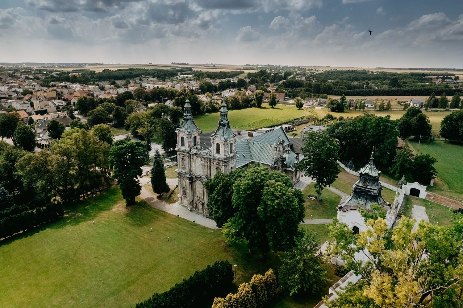 Aerial drone view of stunning Gothic church surrounded by lush green trees and town landscape.