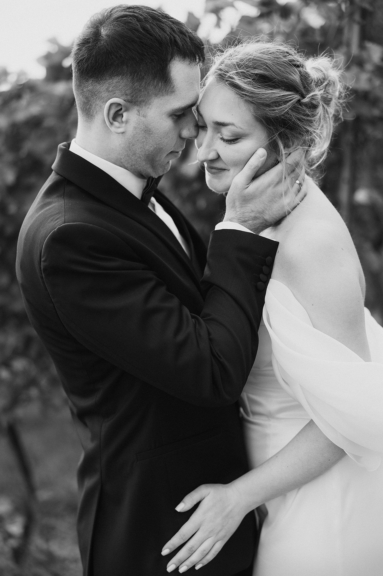 Black and white photo of groom tenderly cupping bride's face as they share an intimate moment outdoors.