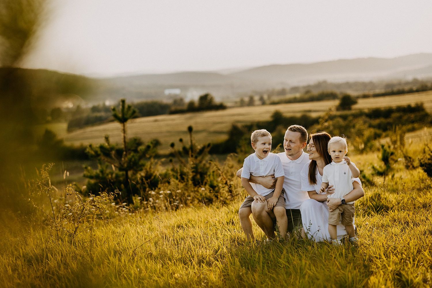 Happy family of four sitting together in sunlit green meadow at golden hour.