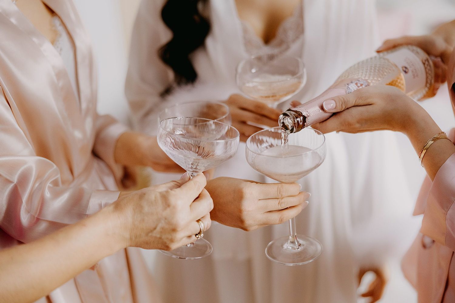 Bridesmaids in pink robes toasting with elegant champagne glasses during bridal party preparations.
