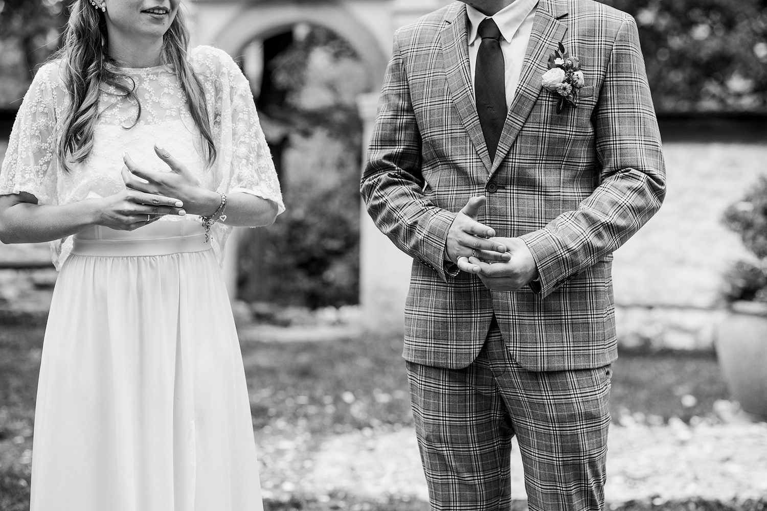 Black and white photo of bride and groom exchanging rings during an outdoor wedding ceremony.
