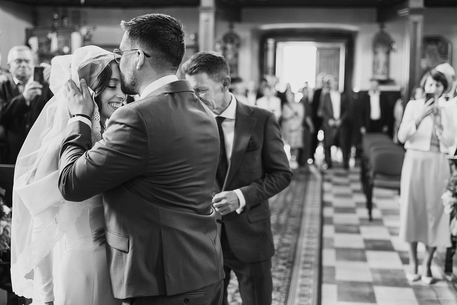 Black and white photo of newlyweds embracing wedding guests in church after ceremony celebration.