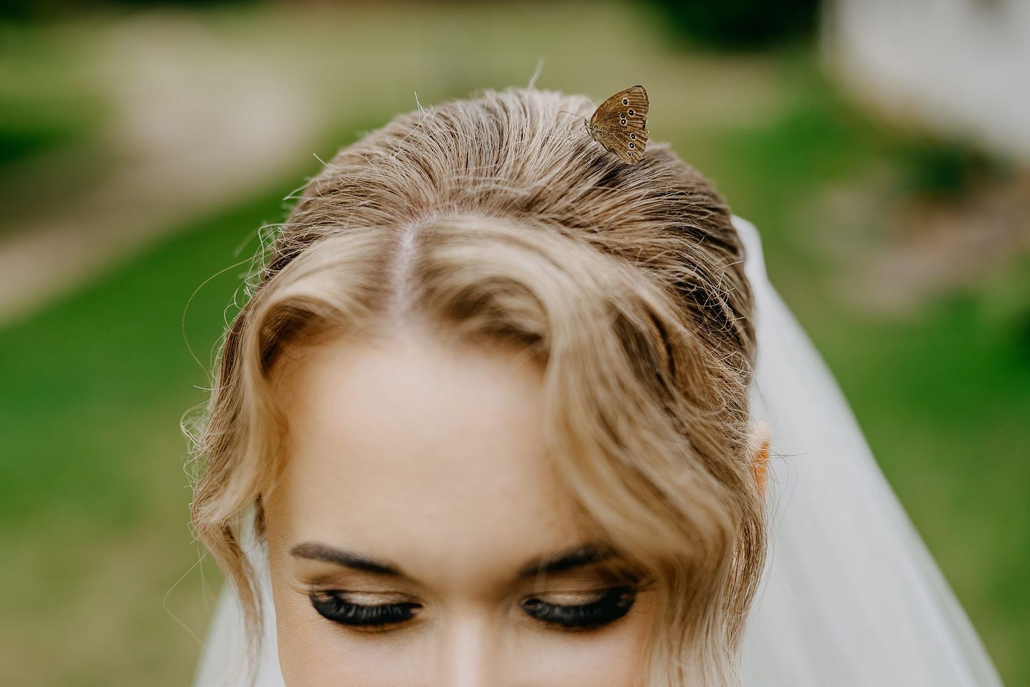 Close-up of bride with elegant updo hairstyle, soft makeup, and delicate wedding veil outdoors.