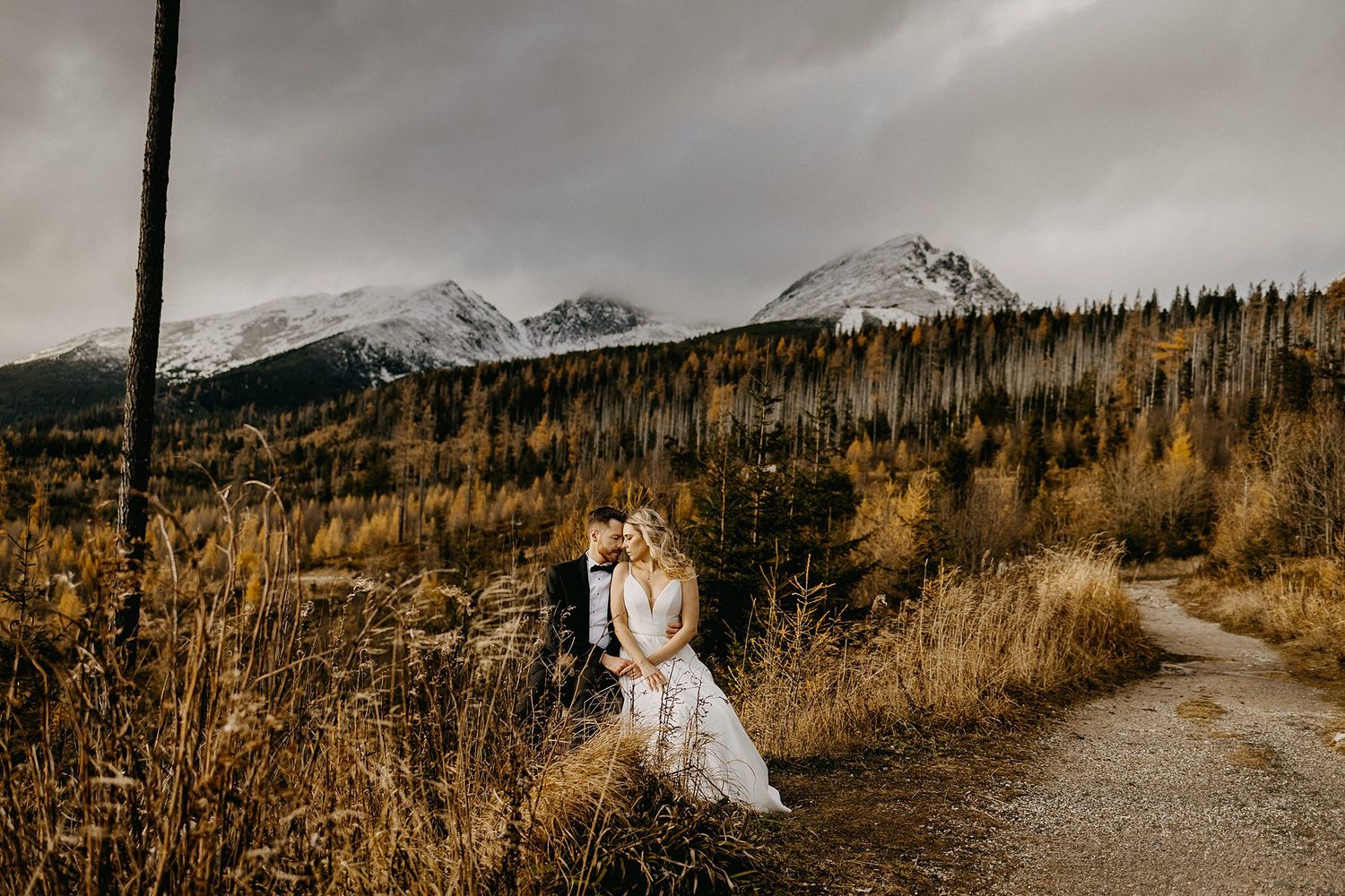 Bride and groom share a tender embrace on a path amid golden autumn mountain scenery.