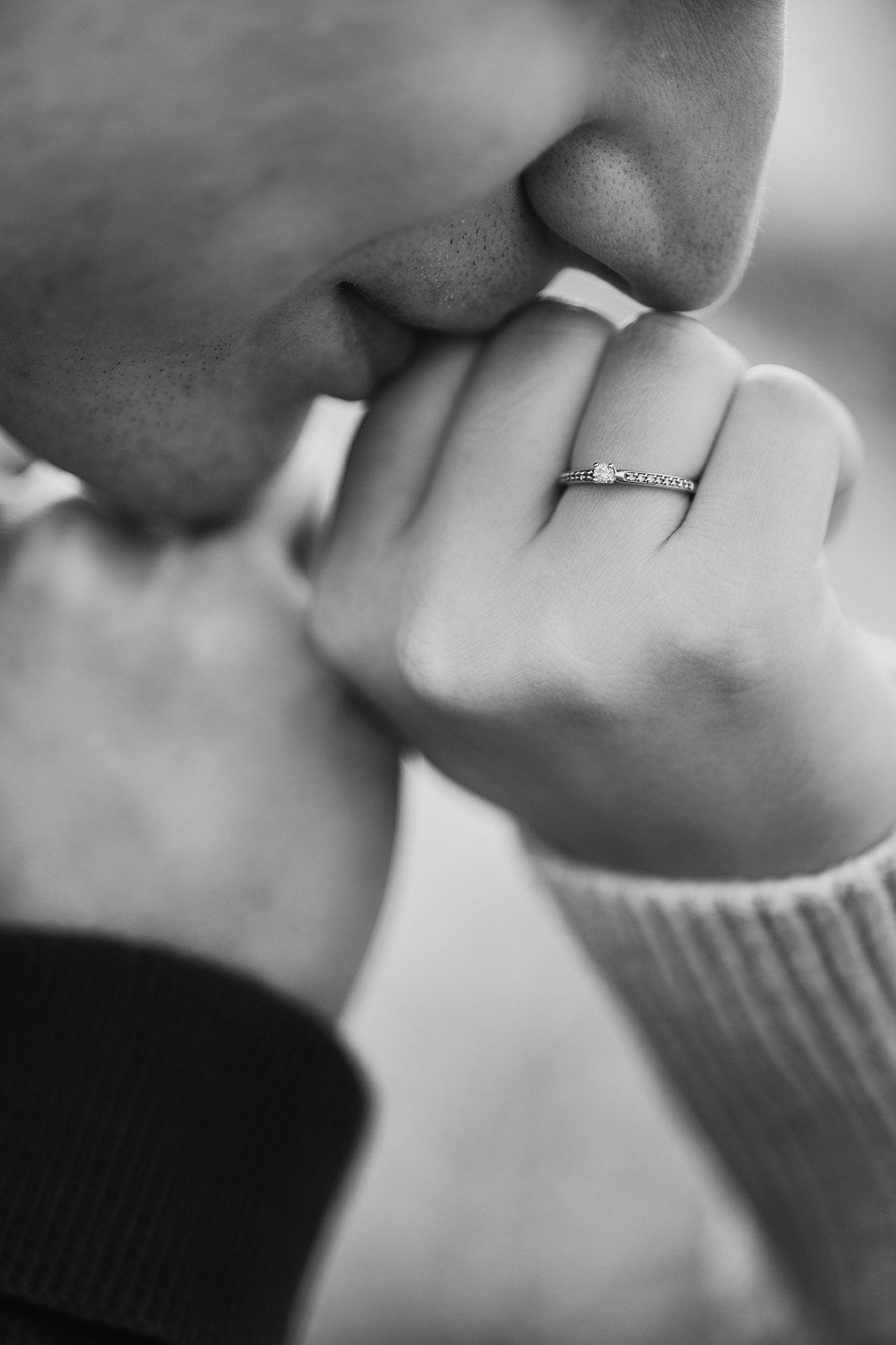 Black and white photo of a man kissing a woman's hand adorned with a diamond engagement ring.